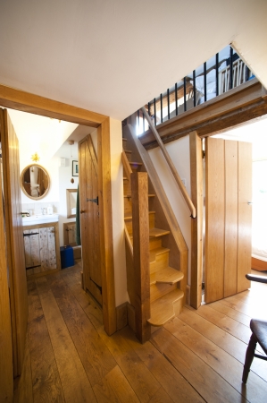A view of a rustic wooden staircase curving upwards, with exposed beams and wood paneled doors inside the characterful cottage.