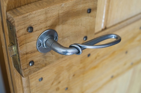 A close-up of an old-fashioned metal door handle on a light wood paneled door.
