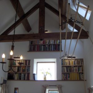 A wooden clothes drying rack suspended up into the high vaulted ceiling with exposed wooden rafters and bookshelves.