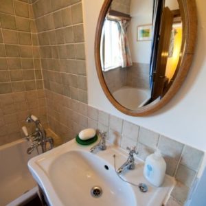 A classic bathroom sink below an oval wooden mirror reflecting the tiled bathtub and shower.