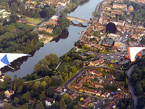 An aerial view of a town beside a winding river with a bridge, taken from a glider showing parts of its wings.