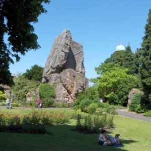 The leaning historic stone ruin of Bridgnorth Castle Keep in a vibrant green park with visitors relaxing on a sunny day.
