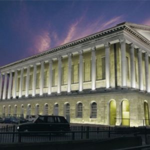 A classically designed building with tall stone columns vividly illuminated at twilight against a dramatic pink and blue sky.