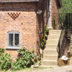 Concrete outdoor stairs beside a brick outbuilding featuring a black metal handrail and a window below.