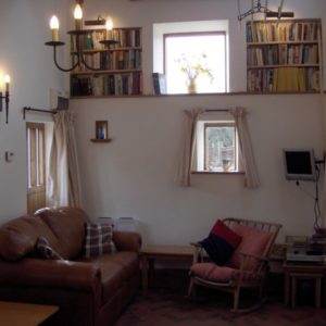 A cozy living space highlighting a brown leather sofa, a wooden rocking chair, and a chandelier below elevated shelves full of books.