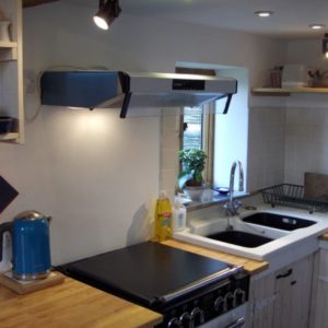 A modern black dual-fuel double oven positioned under a silver extractor hood in a kitchen with wooden countertops and a blue kettle.