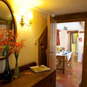 A bright hallway featuring a wooden sideboard with orange flowers, an oval mirror, and a view through an open wooden door into the dining room.