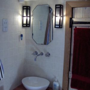 A modern white bowl hand basin in a white tiled bathroom, softly illuminated by two framed wall sconces beside an octagonal mirror.