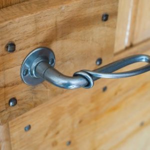 A sturdy vintage metal handle with a curled end mounted on a solid light wood paneled fire door.