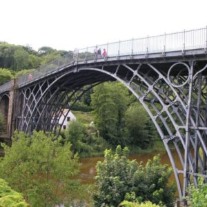 The historic cast iron arch bridge spanning gracefully over a serene river surrounded by green trees.