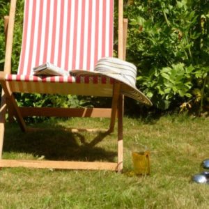 A sunny garden lawn with a striped deckchair, a cool drink, and shiny metallic boules resting on the grass.