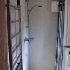A tiled shower cubicle featuring a modern chrome showerhead, a wall-mounted electric shower unit, and a striped curtain.