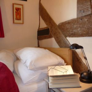 A cozy bedroom setting featuring crisp white pillows on a bed next to rustic exposed diagonal timber framing and a bedside reading lamp.