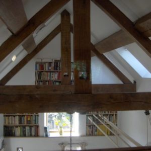 An interior shot showing the grand exposed wooden A-frame roof trusses, skylights, and elevated bookshelves, looking over the living space below.