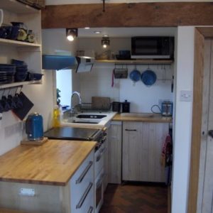 A compact, highly functional kitchen interior equipped with modern appliances including an electric cooker, microwave, kettle, toaster, and wooden countertops.