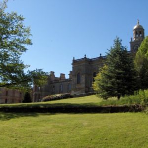 An expansive exterior view of the grand historic ruins of Witley Court on a sunny day set behind a sweeping green lawn.