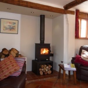 A warmly glowing wood-burning stove positioned between two inviting brown leather sofas on a rich red-tiled floor.